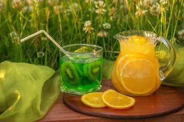 Two glass jars with lemonade on a wooden stand on the grass. Soda in a jar with a lid. Breakfast on the grass.