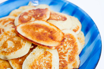 Ruddy freshly cooked pancakes lie on a blue plate on a white background.