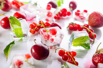 Close up ice cubes with fresh berries among not frozen cherry, strawberry and mint leafs on the white background. Selective focus, Lateral backlight