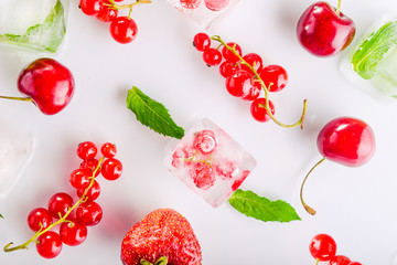 Top view ice cubes with fresh berries among not frozen cherry, strawberry and mint leafs on the white background. Selective focus