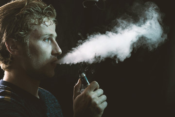 Obraz premium Isolated young man holding and vaping an electronic cigarette or e cig.
