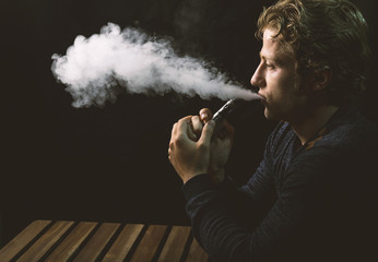 Isolated young man holding and vaping an electronic cigarette or e cig.