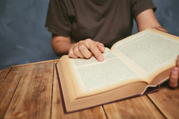 Naklejka premium Senior woman reading a book at living room with old vintage table and concrete wall background.