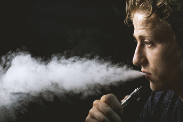 Isolated young man holding and vaping an electronic cigarette or e cig.