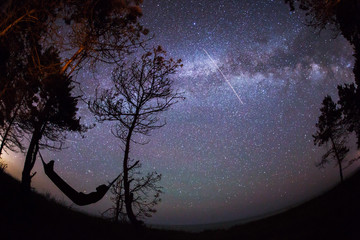 Man sleeping in nature on hammock under the trees with beautiful milky way and stars in background