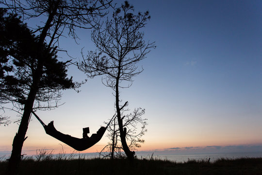 Man reading in nature on hammock under the trees with beautiful sunrise in background