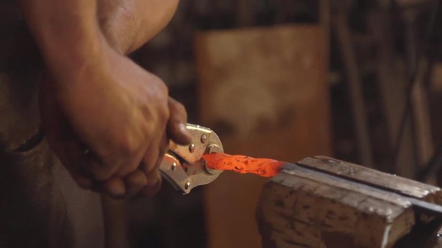Treatment of molten metal close-up. Handmade blacksmith. Man forms a pattern on the iron clamped in the vice. slow motion