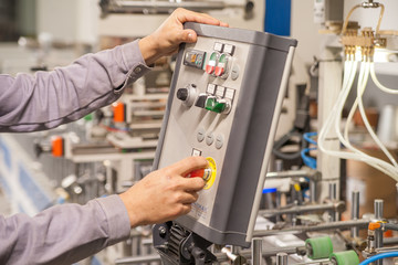 The hands of the male worker on the control panel of the machine