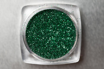 Closeup of green nail makeup glitter in round jar isolated on silver background. Concept of beauty and makeup