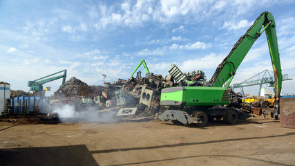 Excavators at work on a scrapheap, some steam coming of a chunk of hot steel