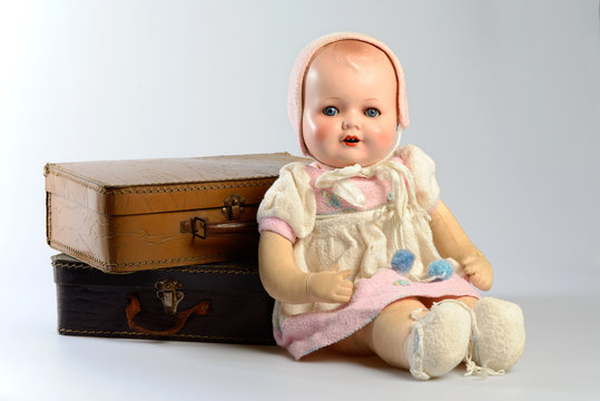 Studio photo of a vintage doll, sitting against two old suitcases