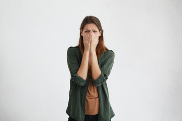 Desperate woman with dark eyes wearing brown T-shirt and green jacket going to cry after hearing horrified news isolated over white background. Tragic emotions, feelings, facial expressions concept