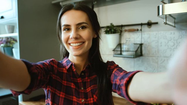 Attractive smiling woman making selfies, photos on her device in the kitchen at home. Close up.