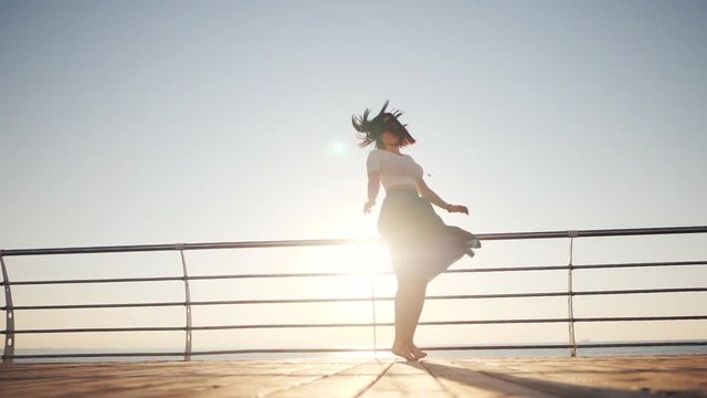 The spinning around woman in retro style long skirt on sunrise background near sea or ocean. Joy and happiness. Slow motion.