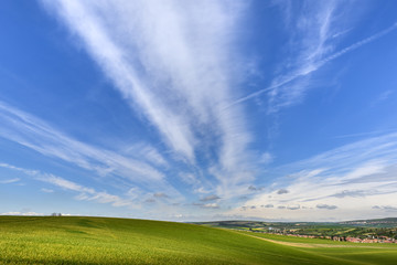 Wavy green field with cloudy blue sky and small village