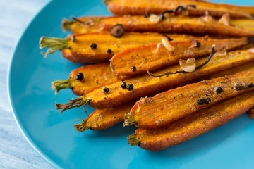 Roasted spring carrots on blue plate with garlic, pepper peas and coriander on wooden table. Selective focus