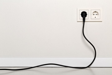 Black power cord cable plugged into european wall outlet on white plaster wall - obrazy, fototapety, plakaty