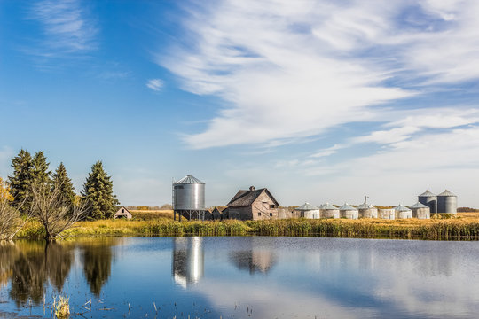 old farm yard with grain bins and a pond in the foreground