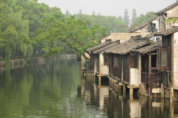 Fototapeta na wymiar Wooden, weathered buildings lining the water canals in tongxiang wuzhen scenic town east view in Zhejiang province China in the early morning mist.