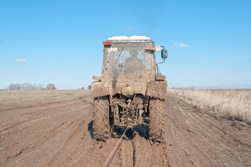 Wheeled tractor tows in mud on dirt road in fallow field

