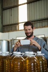 Smiling working taking a photo of olive oil bottles