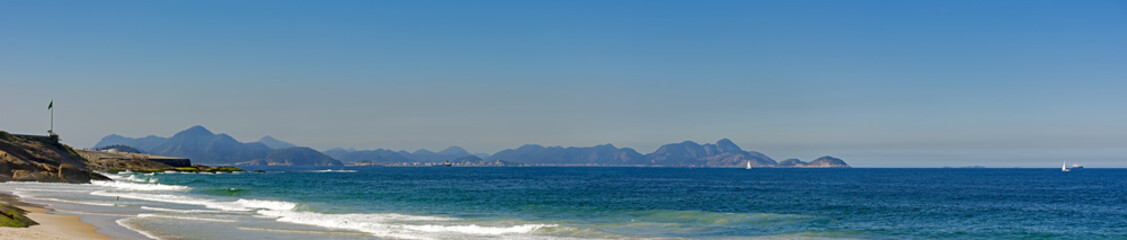 Fototapeta na wymiar Panoramic view of Devil's beach and the Copacabana fort with brazilian flag and the hills of the city of Niteroi in the background