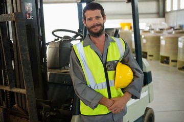 Smiling worker standing near forklift in factory