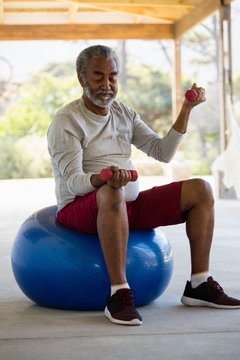 Senior Man Exercising With Dumbbells On Exercise Ball In The Porch