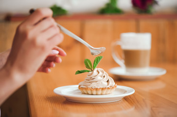 Woman eating a cake of cottage cheese in a ceramic plate with a spoon on a wooden table