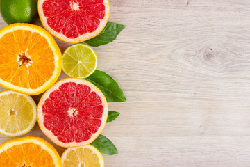 Juicy citrus fruits cut background mint leaf. Oranges, lemons, limes, grapefruit, mint leaves on a bright wooden background