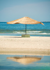 Straw umbrella against the sun on the beach with reflection in the bay of the sea