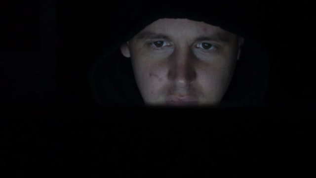Male hacker working on a computer in a dark office room.