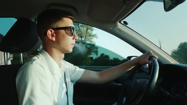 A young man smokes an electronic cigarette, drives a car