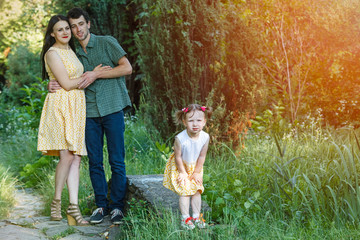 Fototapeta premium In foreground a girl is standing with his hands on his knees. In background parents embracing each other looking at her.