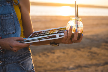 Obraz premium Young woman artist painting landscape in the open air on the beach, close up