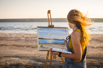 Fototapeta premium Young woman artist painting landscape in the open air on the beach