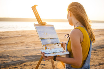 Naklejka premium Young woman artist painting landscape in the open air on the beach