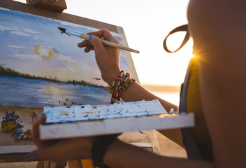 Young woman artist painting landscape in the open air on the beach, close up