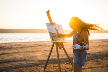 Young woman artist painting landscape in the open air on the beach - 162772332