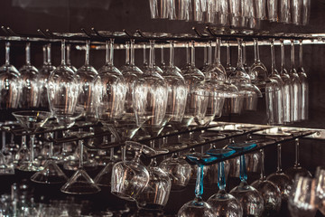 raws of glasses for a margarita, martini, grog and liqueur hanging upside down in bar at arestaurant, dark background.