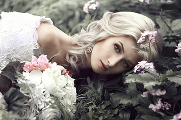 Portrait of a beautiful young woman as a princess lies in a forest with flowers.