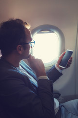 Man using smartphone in the airplane and looking throught the window.