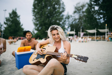 Group of attractive young people enjoying holiday beach fun while beautiful blonde woman playing guitar.