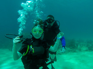 Naklejka na ściany i meble A couple scuba dive together. A female scuba diver with the regulator out. Smiling, holding the regulator. Divers. Roatan, Honduras