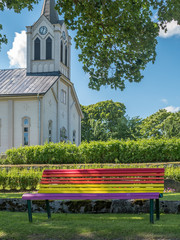 Rainbow flag colors on bench, church in background. Gay marriage concept.