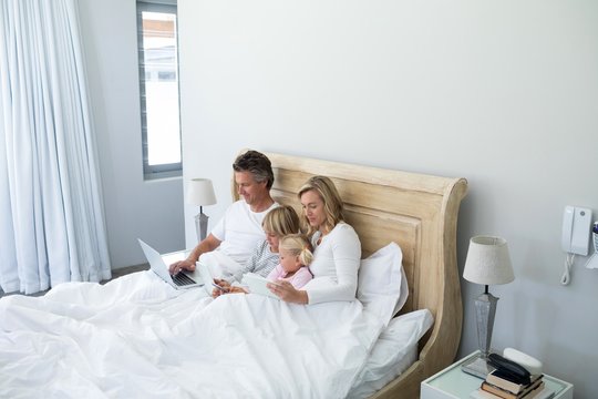 Family using digital tablet, mobile phone and laptop on bed in t