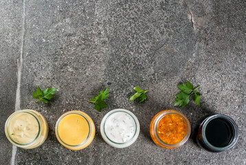 Set of organic healthy dietary dressings for salad: sauce vinaigrette, mustard, mayonnaise with spices or ranch, balsamic or soy, basil with yogurt. On a dark stone table. Top view copy space