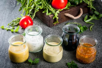 Foto op Plexiglas Set of dressings for salad: sauce vinaigrette, mustard, mayonnaise or ranch, balsamic or soy, basil with yogurt. Dark stone table. On background of greenery, vegetables for salad. Copy space © ricka_kinamoto