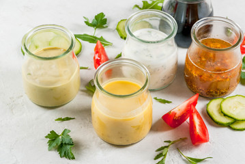 Set of dressings for salad: sauce vinaigrette, mustard, mayonnaise or ranch, balsamic or soy, basil with yogurt. Dark white concrete table, with greenery, vegetables for salad. Copy space
