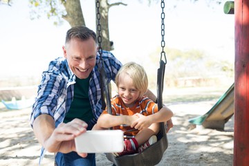 Father taking selfie with son sitting on swing - Powered by Adobe